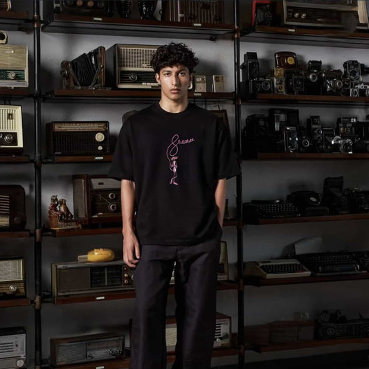 Person wearing a black t-shirt with a graphic design in a room with vintage electronic equipment.